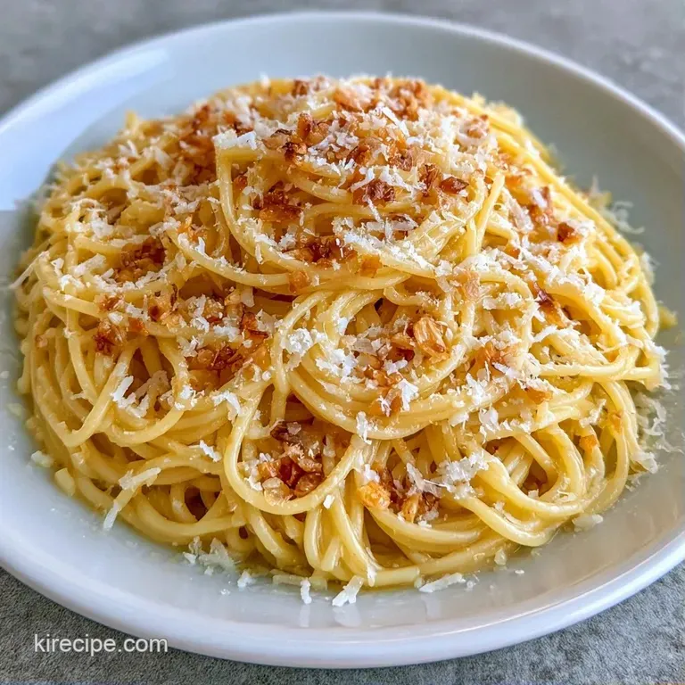 Elegant plating of buttery pasta topped with grated parmesan cheese and a sprig of herbs on a dark slate platter.