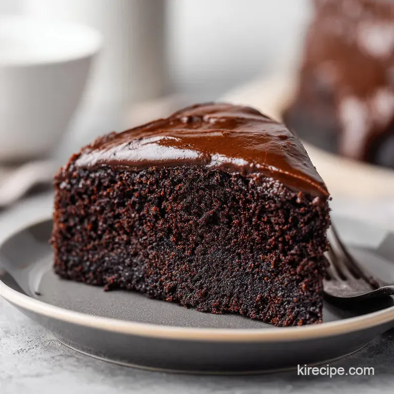 A slice of dark, moist cake paired with a swirl of raspberry coulis and a fresh mint leaf on a slate platter.