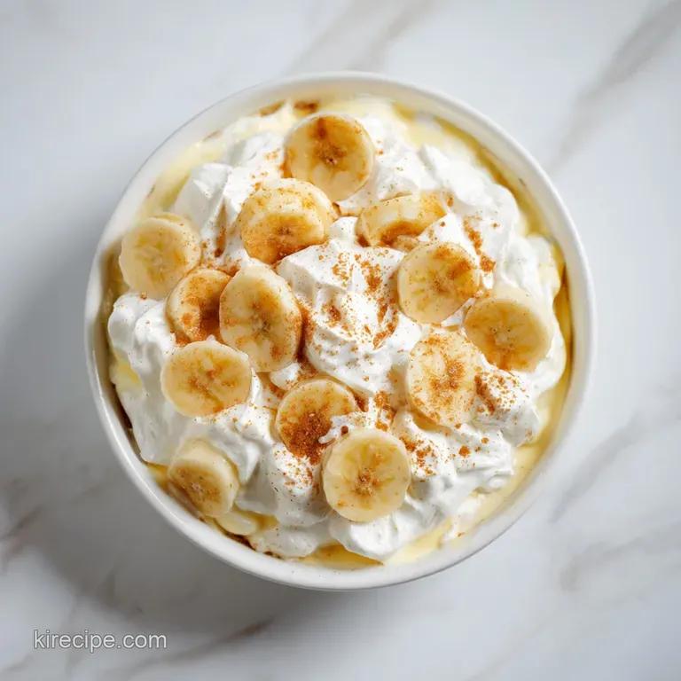 A single serving of banana pudding artfully spooned into a dessert glass, topped with whipped cream and a wafer shard.