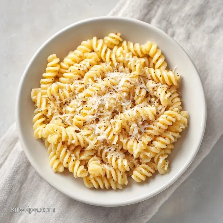 Elegant white platter piled high with glossy rotini pasta, dusted with snow-white parmesan and fresh parsley.
